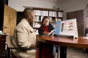 This image depicts a person with diabetes in the foreground, listening to a community health worker.