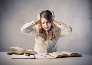 An image of a person sitting at a table with a notebook and open textbooks. The person appears stressed.