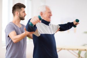 A physical therapist assists an elderly patient exercise.