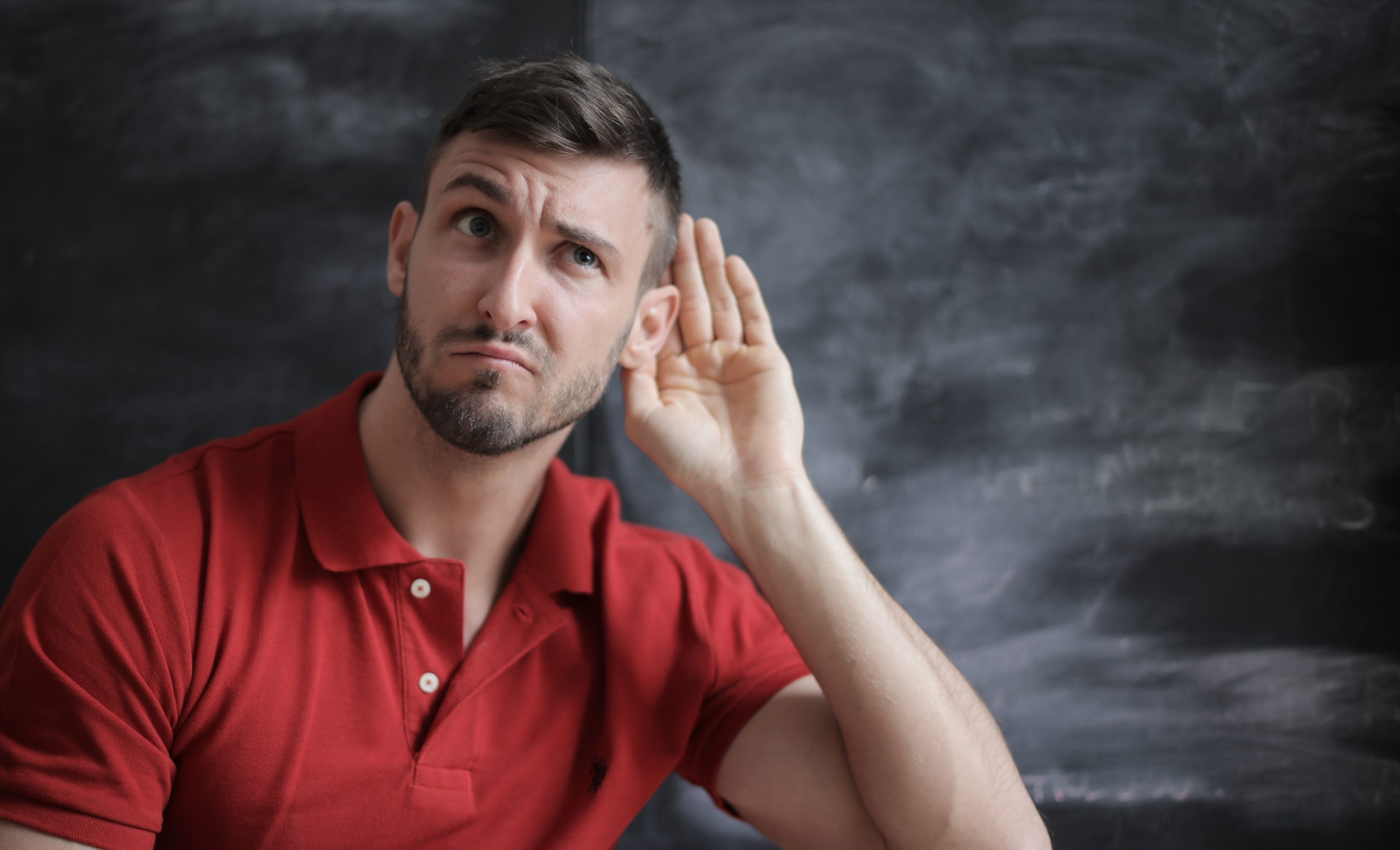 A man leaning to the side with his hand next to his ear in a listening pose.