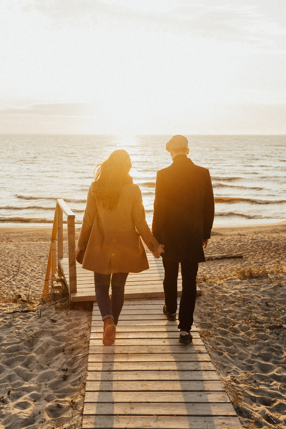 A man and woman walk down a boardwalk, holding hands.