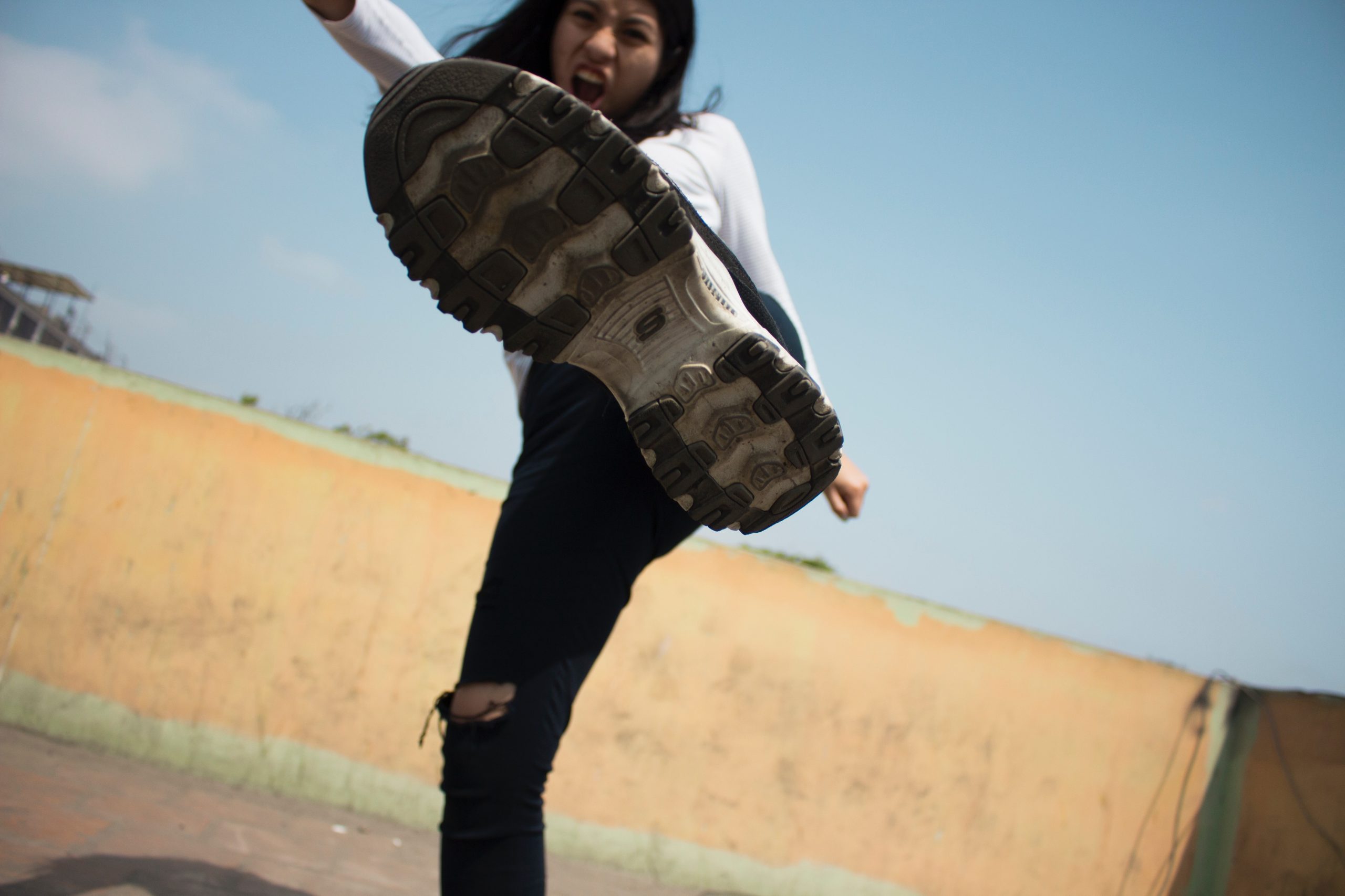 A woman kicking out with the underside of her sneaker in the forefront of the image.